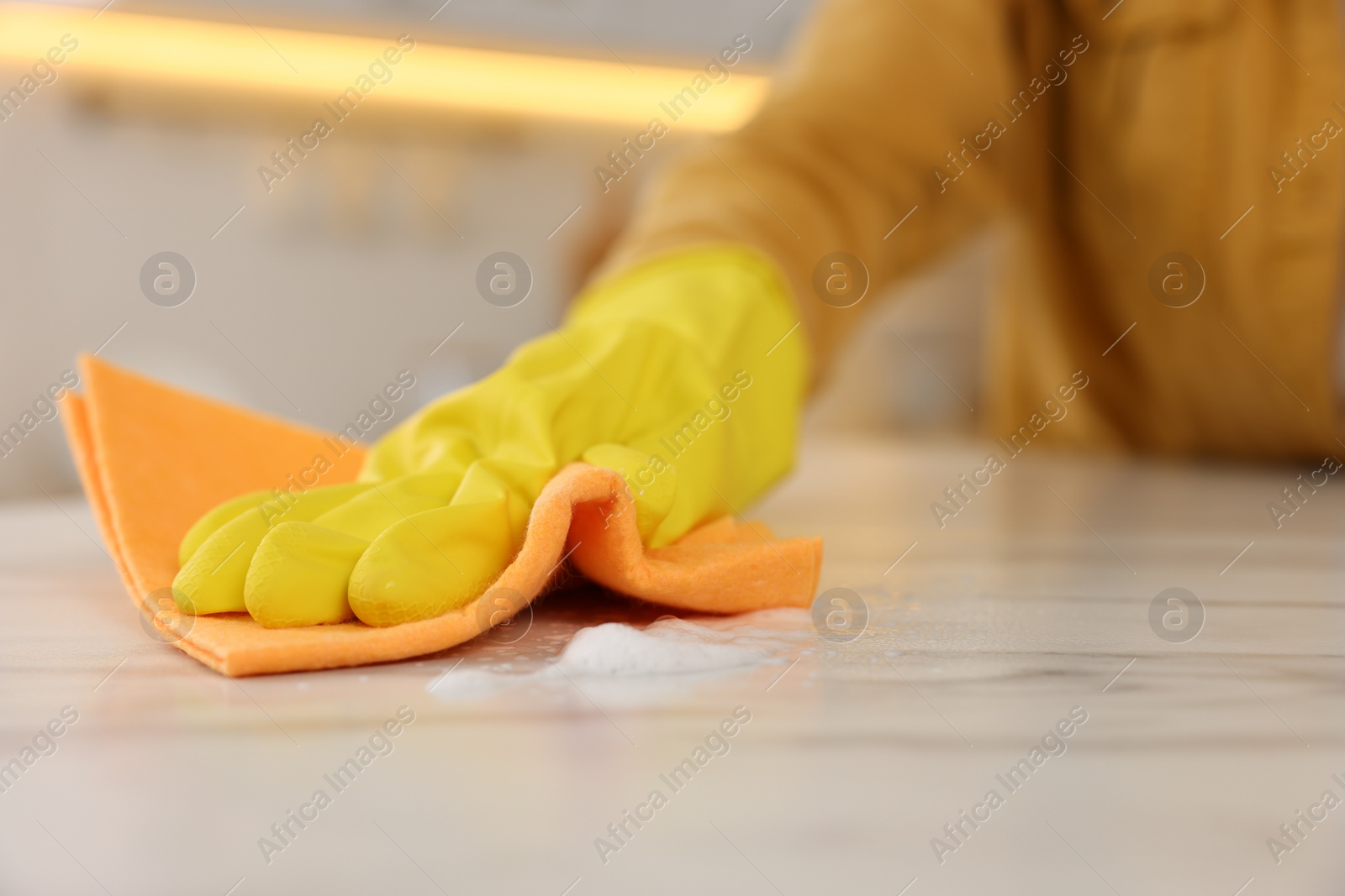 Photo of Woman with microfiber cloth cleaning white marble table in kitchen, closeup