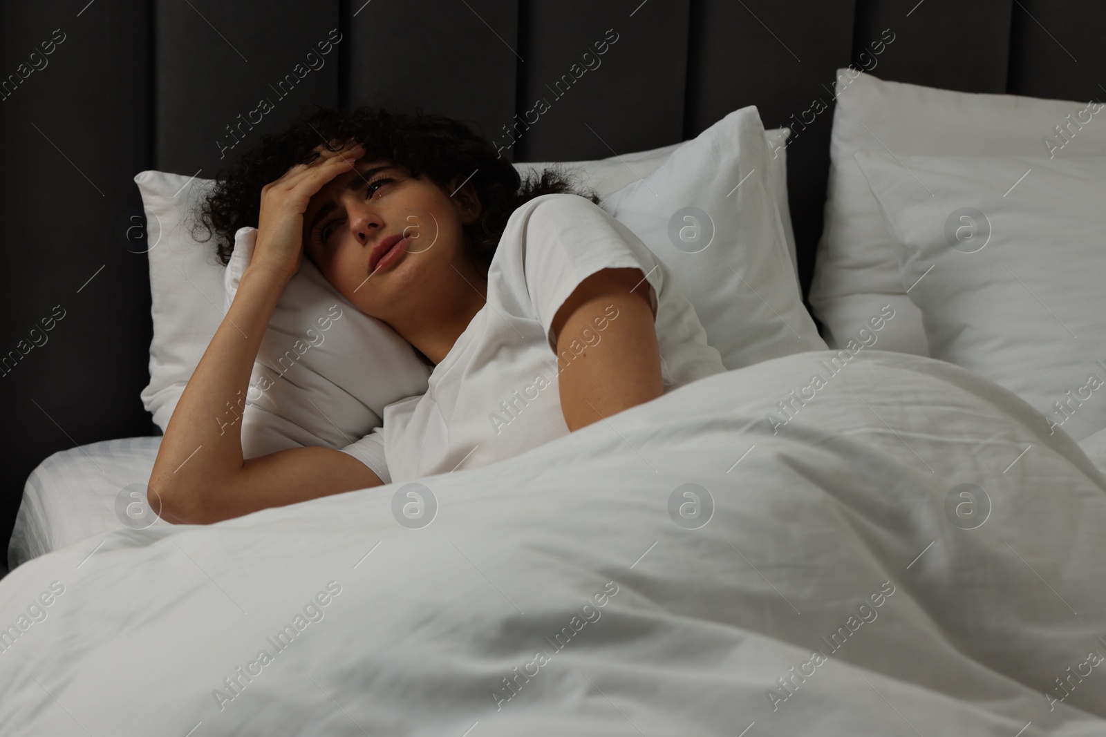 Photo of Young woman suffering from headache in bed at night