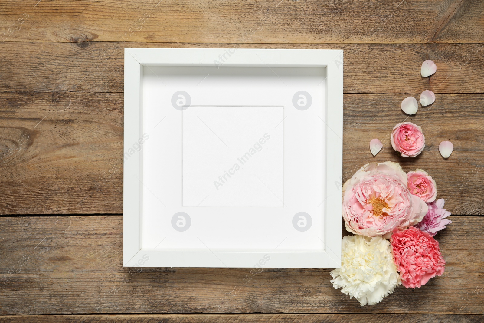 Photo of Empty photo frame and beautiful flowers on wooden table, flat lay. Space for design