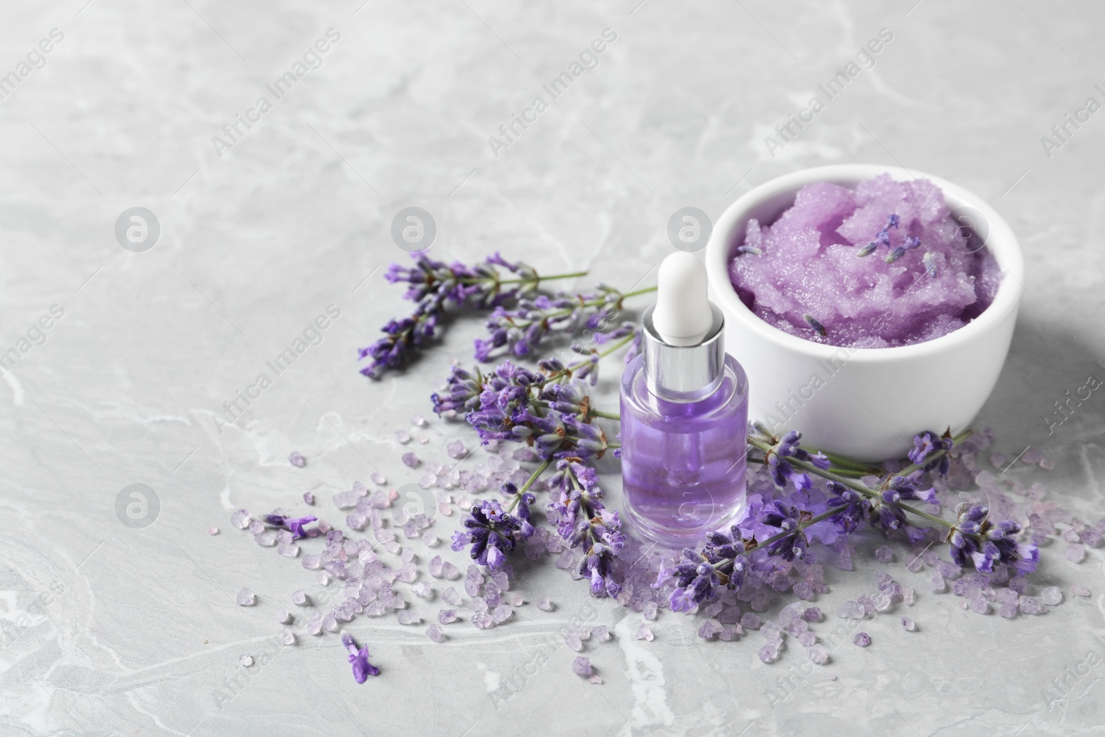 Photo of Natural cosmetic oil, bath salt, scrub and lavender flowers on grey marble table, space for text