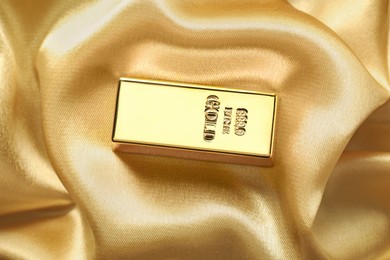 Photo of Gold bar on shiny silk fabric, top view