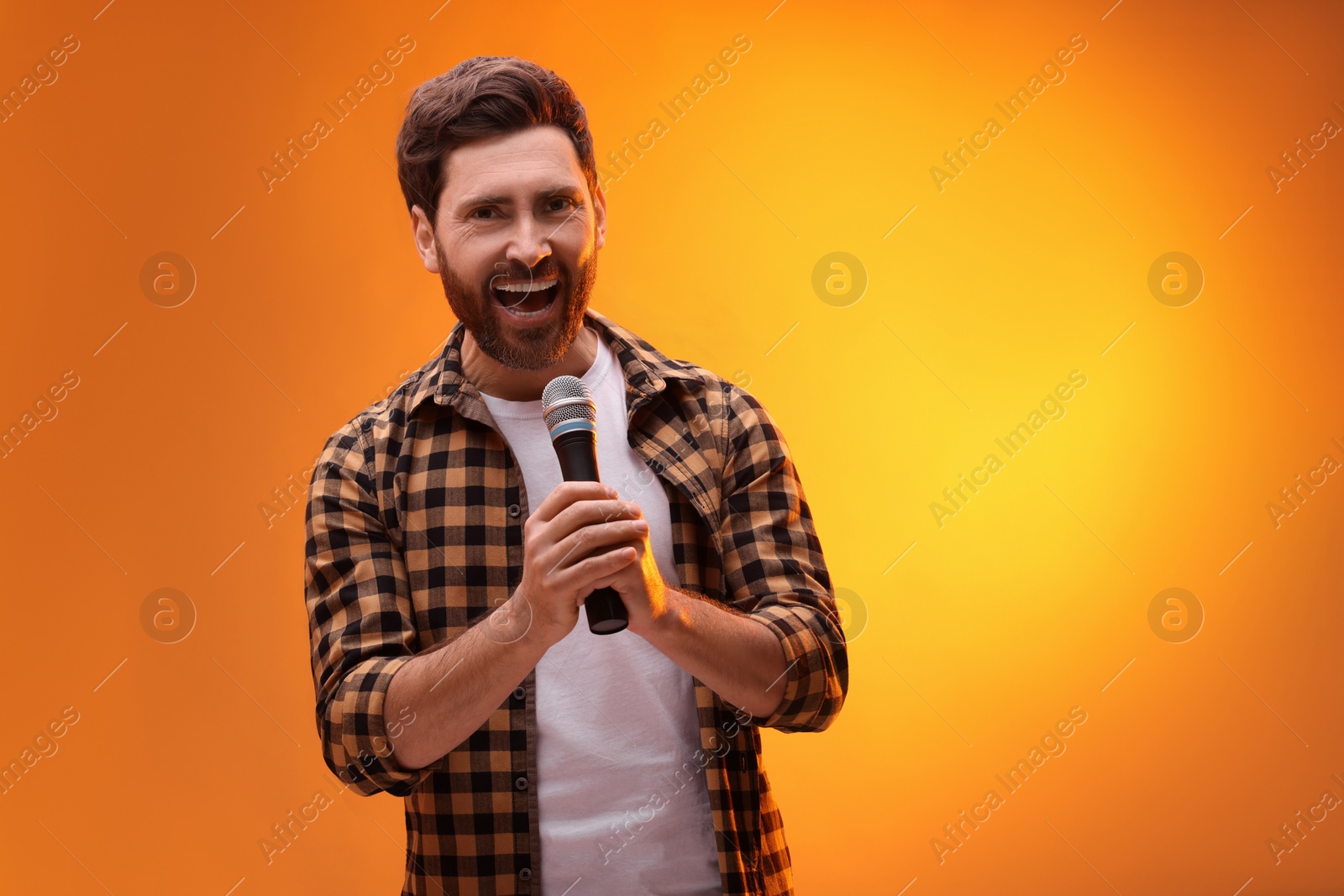 Photo of Handsome man with microphone singing on golden background. Space for text