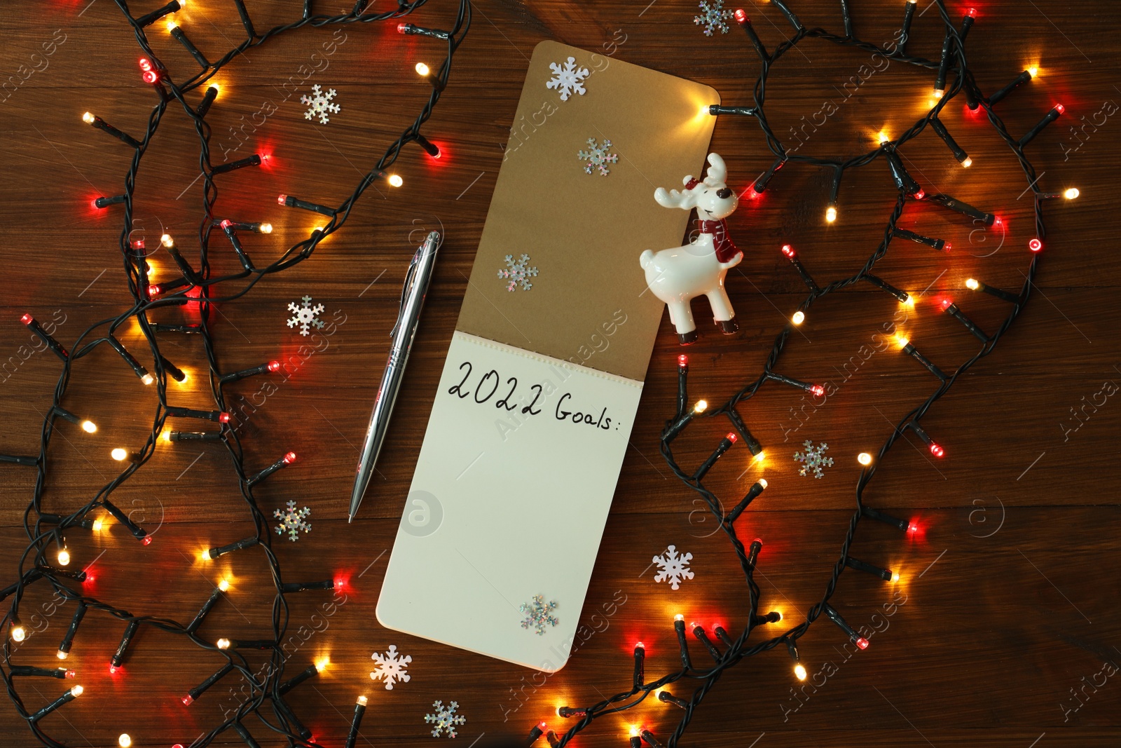 Photo of Inscription 2022 Goals written in planner and Christmas decor on wooden background, flat lay. New Year aims