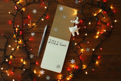 Photo of Inscription 2022 Goals written in planner and Christmas decor on wooden background, flat lay. New Year aims