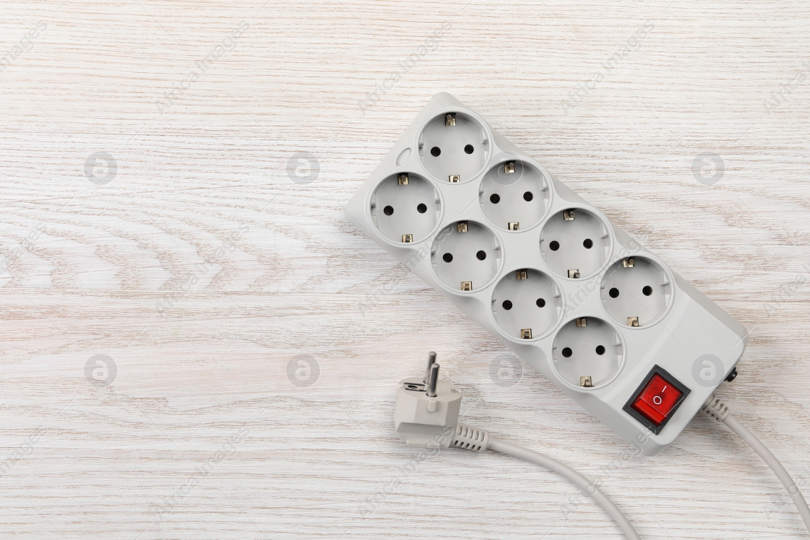 Photo of Power strip with extension cord on white wooden floor, top view. Space for text