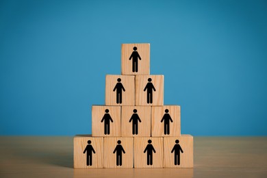 Team and management concept. Pyramid of wooden cubes with human icons on table against light blue background