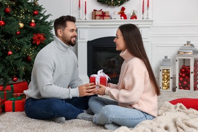 Photo of Happy man presenting Christmas gift to his girlfriend at home