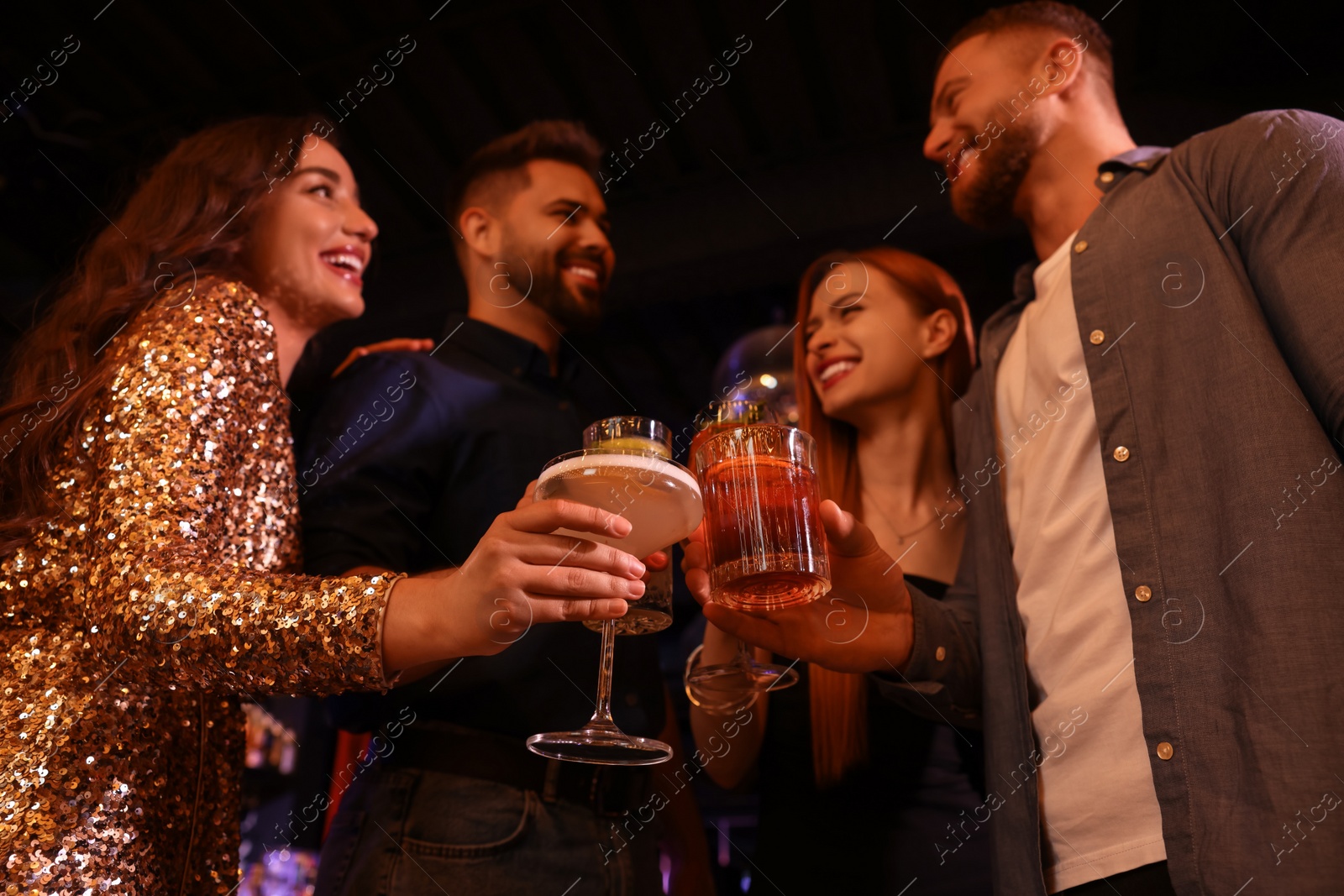 Photo of Happy friends clinking glasses with fresh cocktails in bar, low angle view