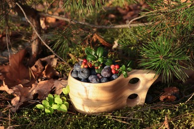 Photo of Wooden mug full of fresh ripe blueberries and lingonberries on grass