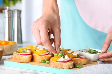 Photo of Woman preparing bruschettas at white marble table, closeup