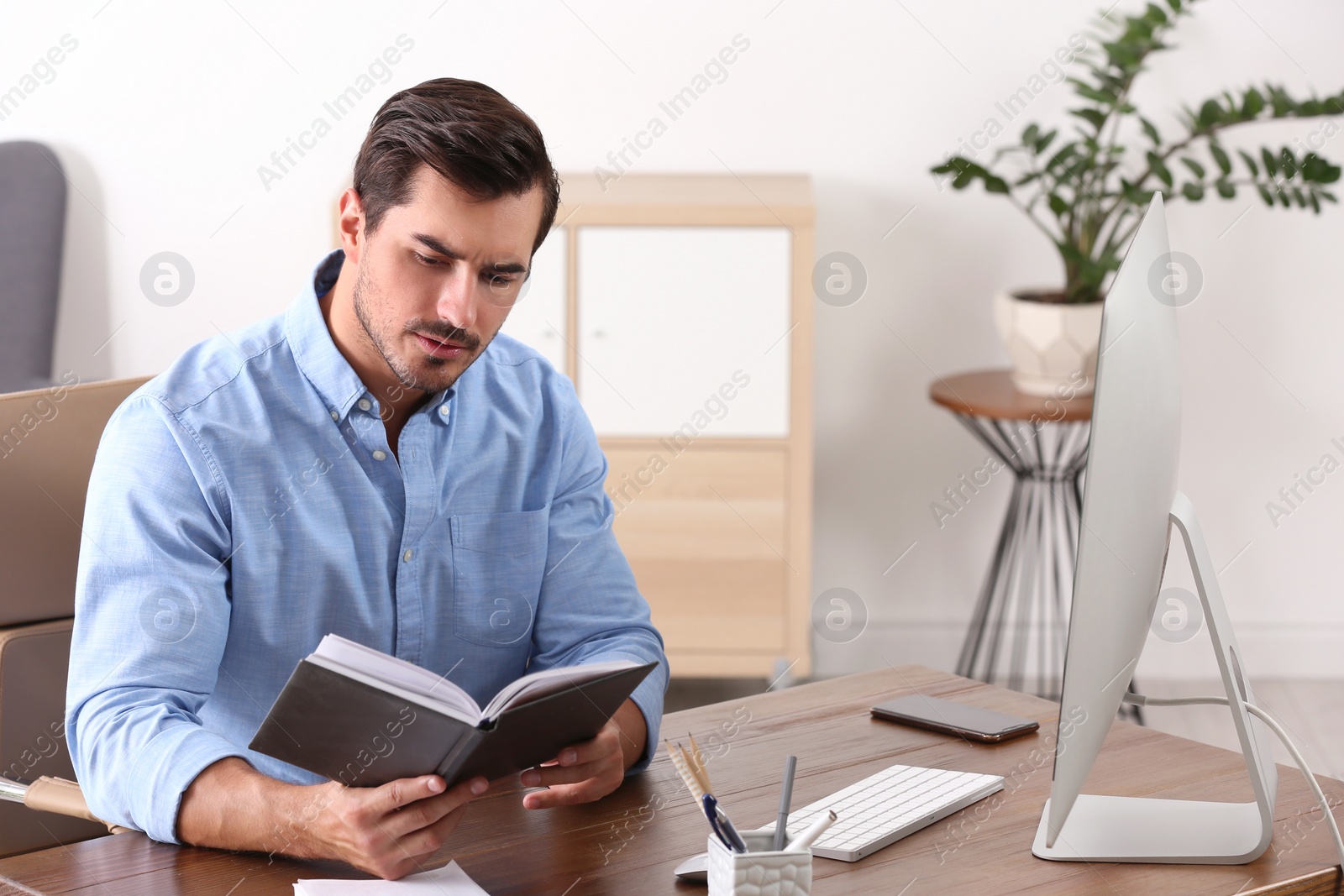 Photo of Handsome young man working with notebook and computer at table in office