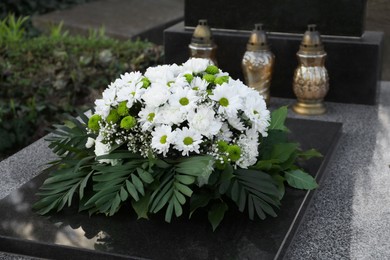 Funeral wreath of flowers and grave lanterns on granite tombstone in cemetery