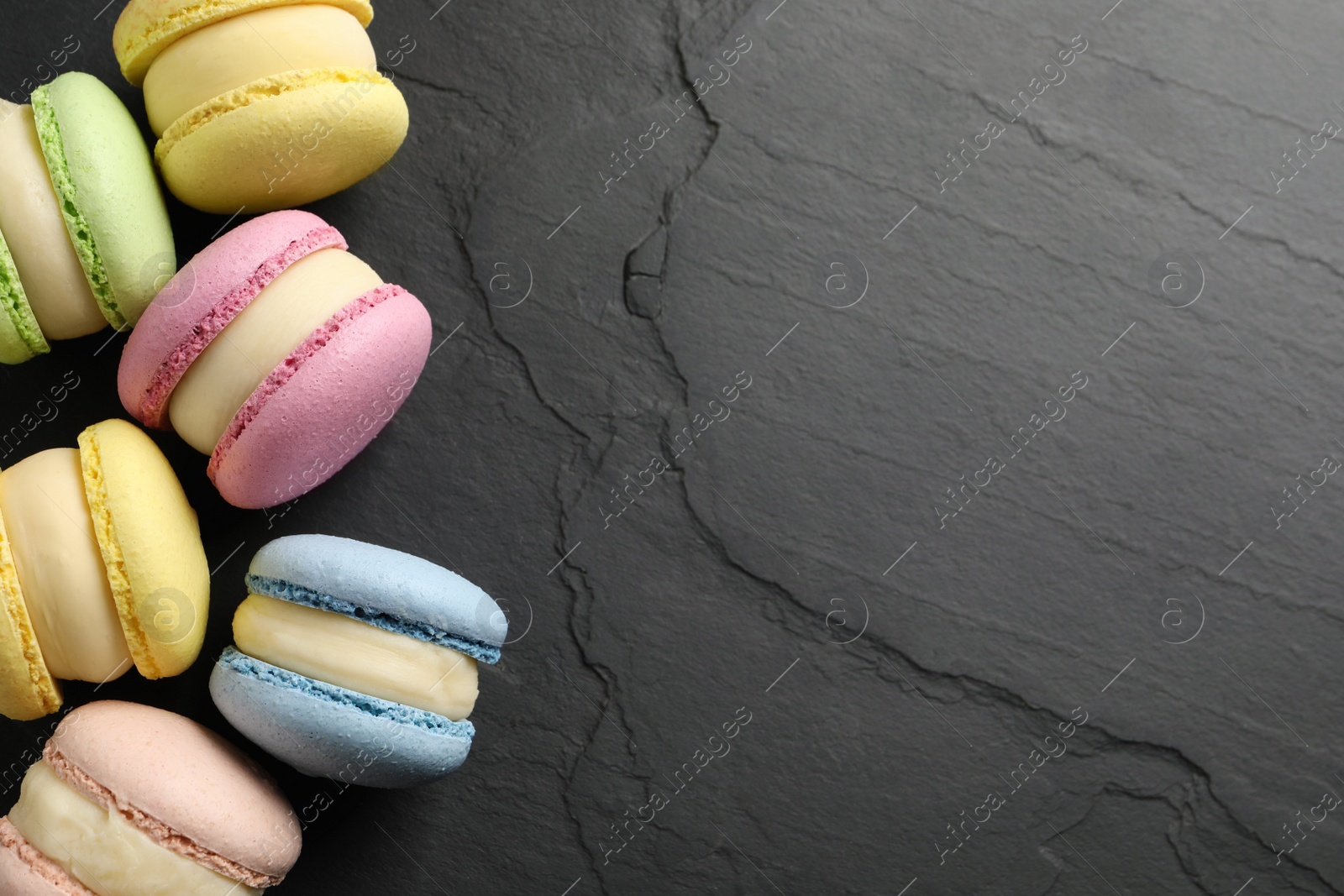 Photo of Delicious colorful macarons on black table, flat lay. Space for text