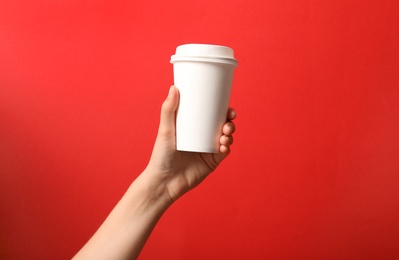 Photo of Woman holding takeaway paper coffee cup on red background, closeup