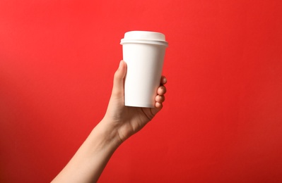 Woman holding takeaway paper coffee cup on red background, closeup