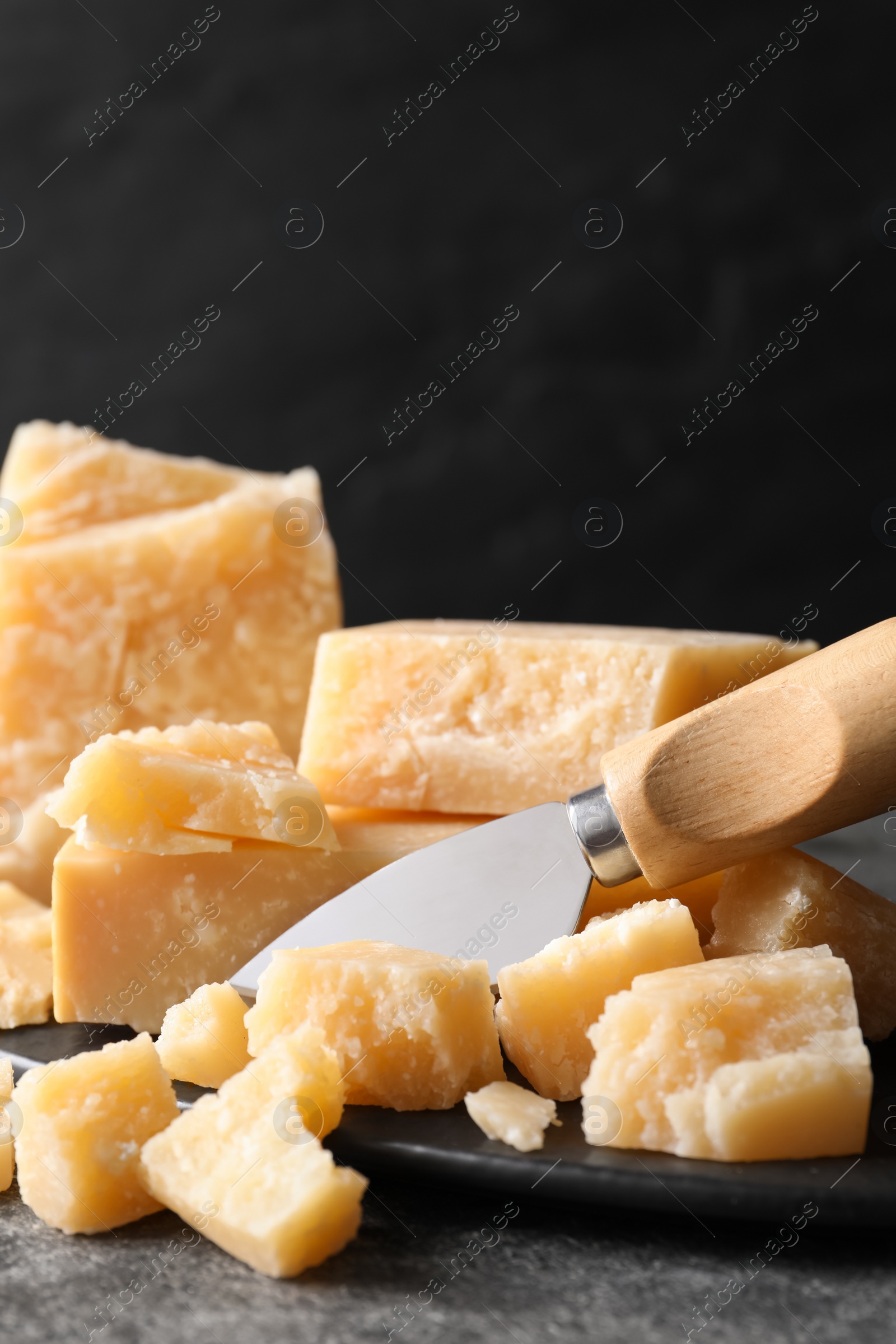 Photo of Parmesan cheese with board and knife on grey table, closeup