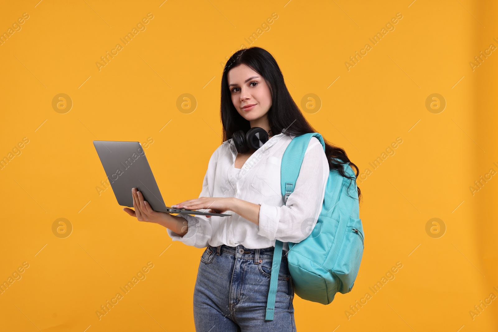 Photo of Student with laptop and backpack on yellow background