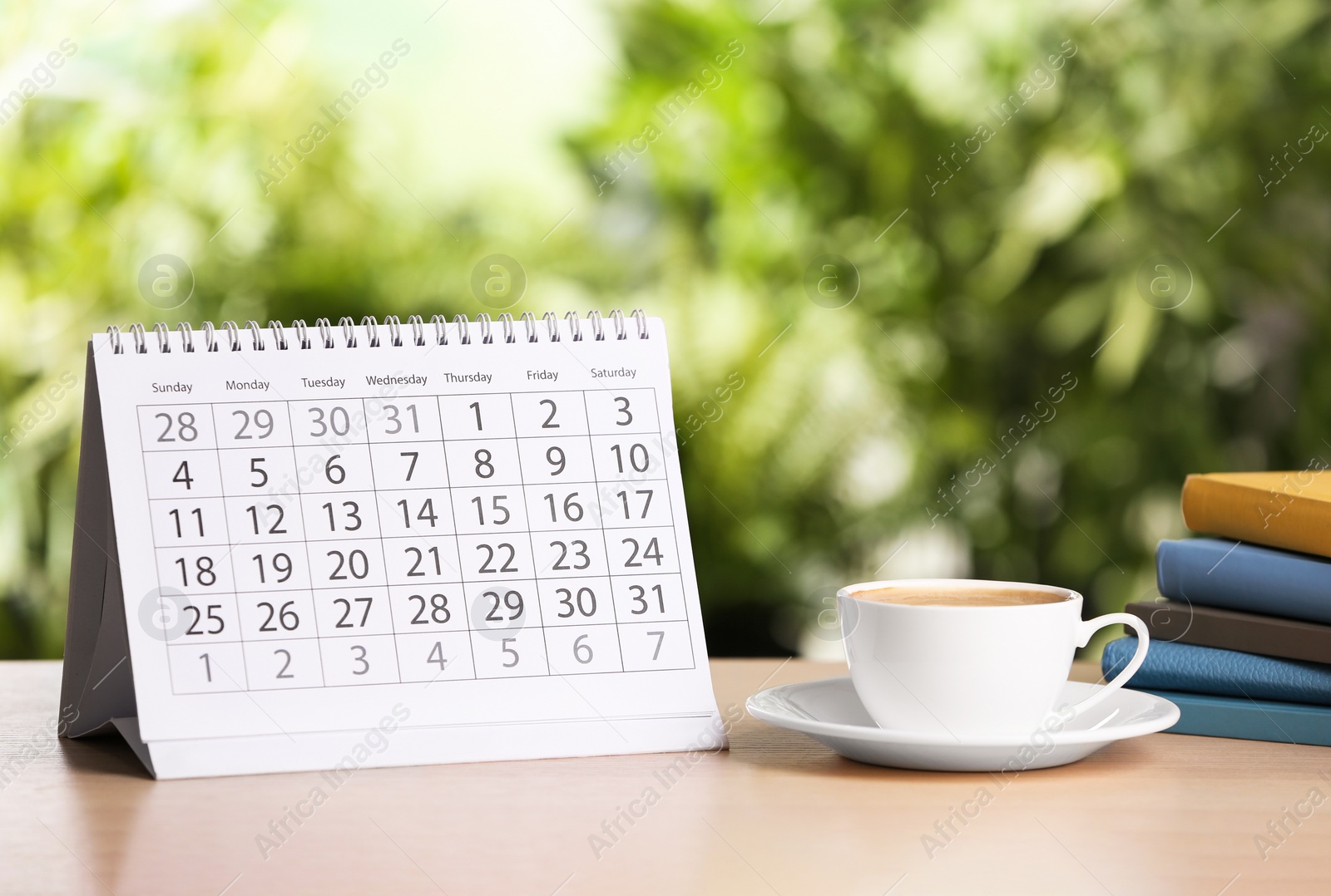 Photo of Calendar and cup of coffee on wooden table against blurred background