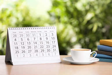 Photo of Calendar and cup of coffee on wooden table against blurred background