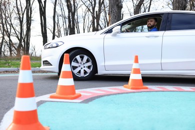 Young man in car on test track with traffic cones. Driving school