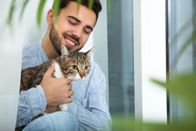 Photo of Man with tabby cat near window at home. Friendly pet