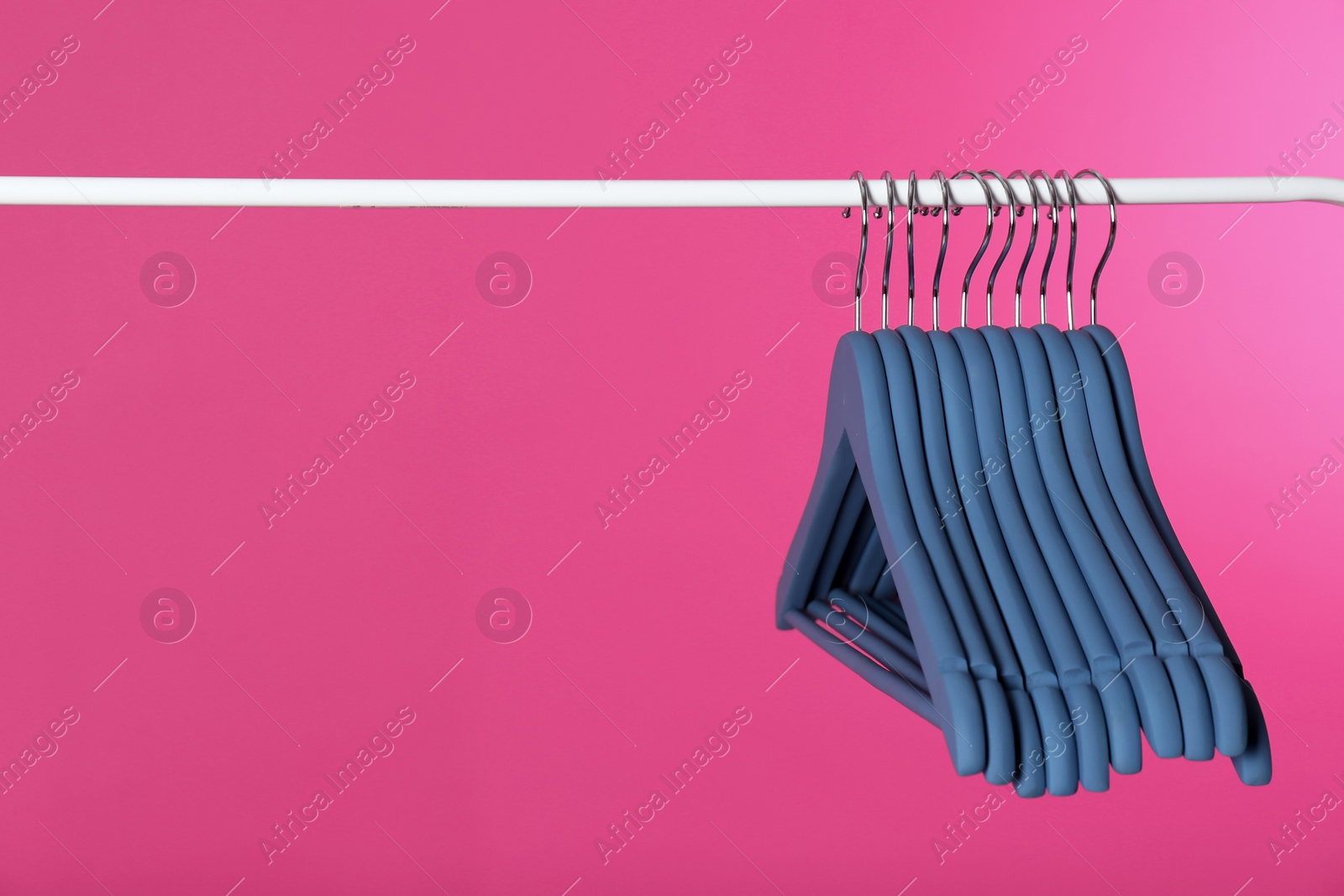 Photo of Metal rack with clothes hangers on color background, space for text