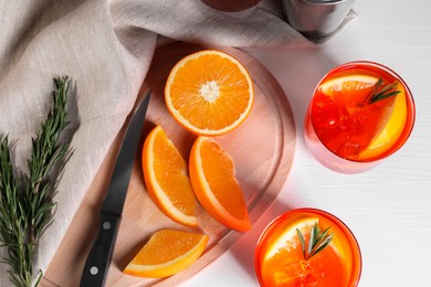 Photo of Aperol spritz cocktail, rosemary and orange slices on white table, flat lay