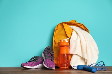 Sports bag and gym equipment on wooden floor against color background