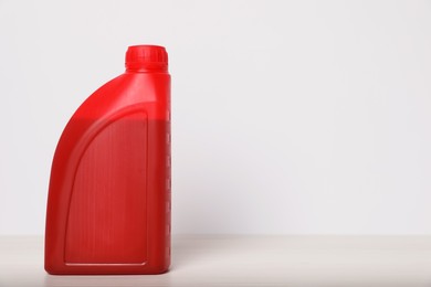 Motor oil in red canister on table against white background, space for text