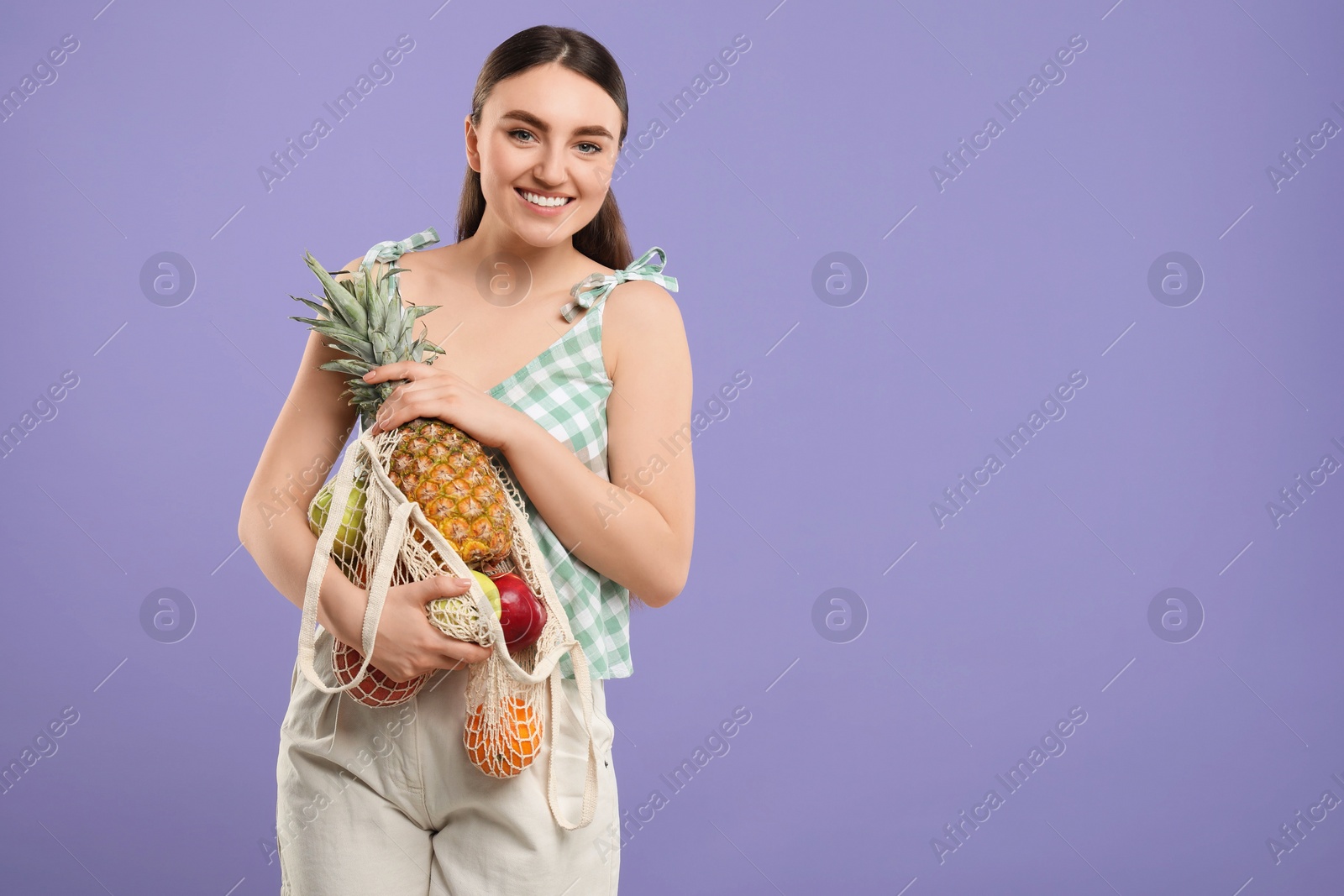 Photo of Woman with string bag of fresh fruits on violet background, space for text