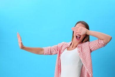 Young woman covering eyes with hands on blue background