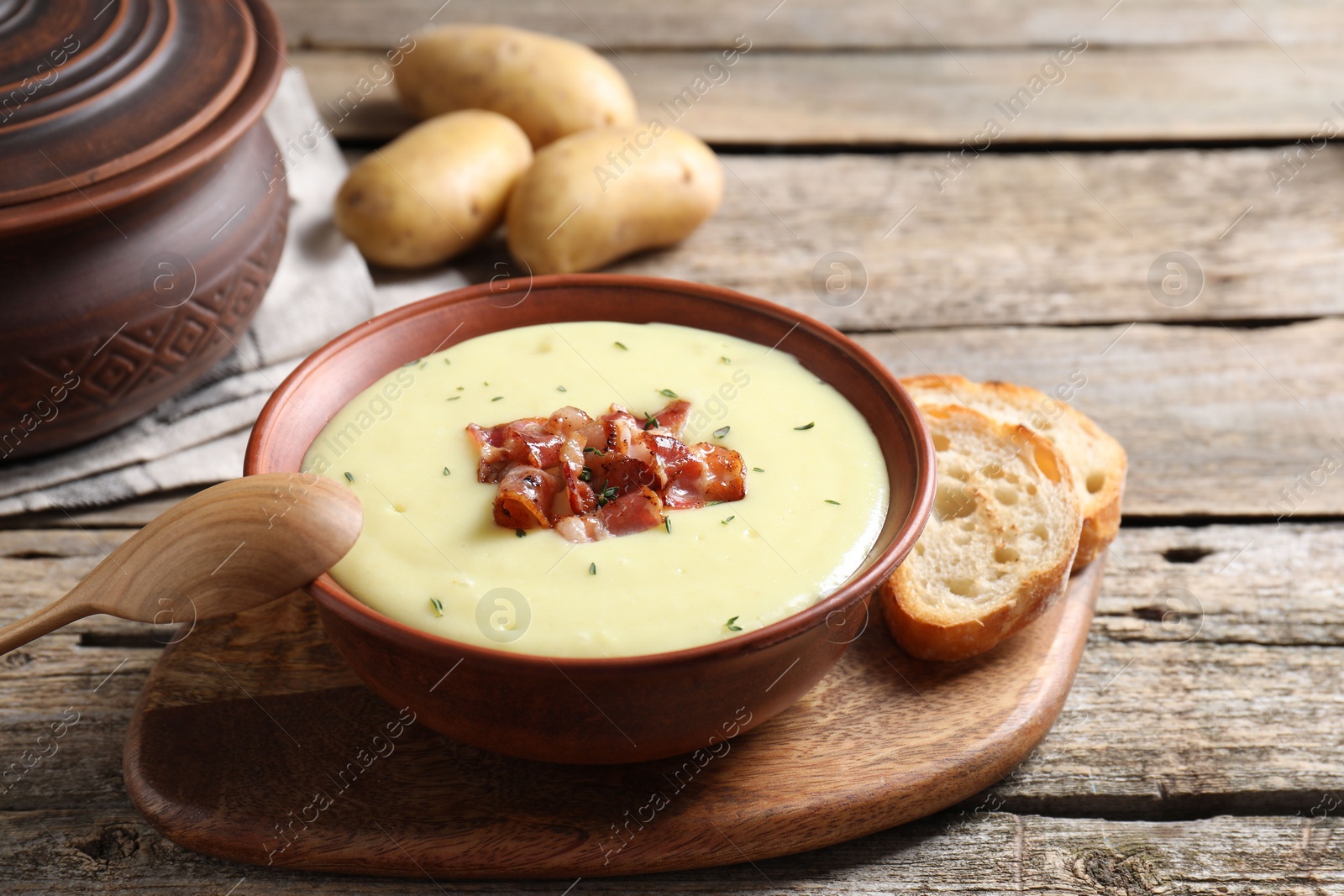 Photo of Tasty potato soup with bacon and rosemary in bowl served on wooden table