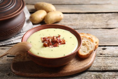 Tasty potato soup with bacon and rosemary in bowl served on wooden table