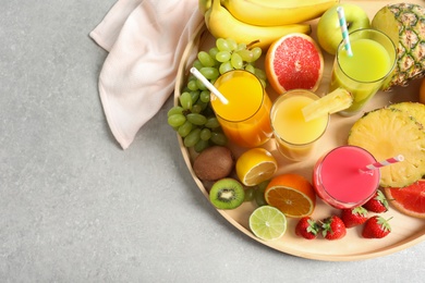 Wooden tray with glasses of different juices and fresh fruits on table, top view. Space for text