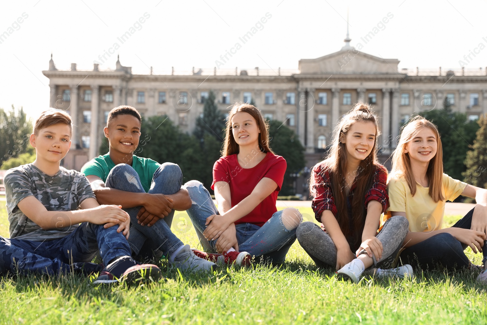 Photo of Group of children sitting on grass outdoors. Summer camp