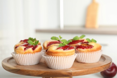 Photo of Delicious sweet cupcakes with plums on wooden stand, closeup