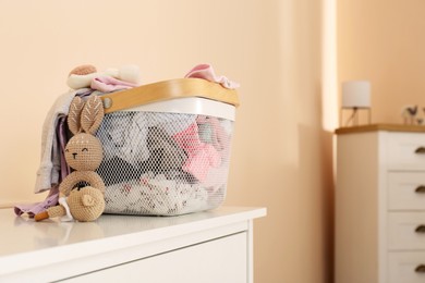 Photo of Laundry basket with baby clothes and crochet toys on white chest of drawers indoors, space for text