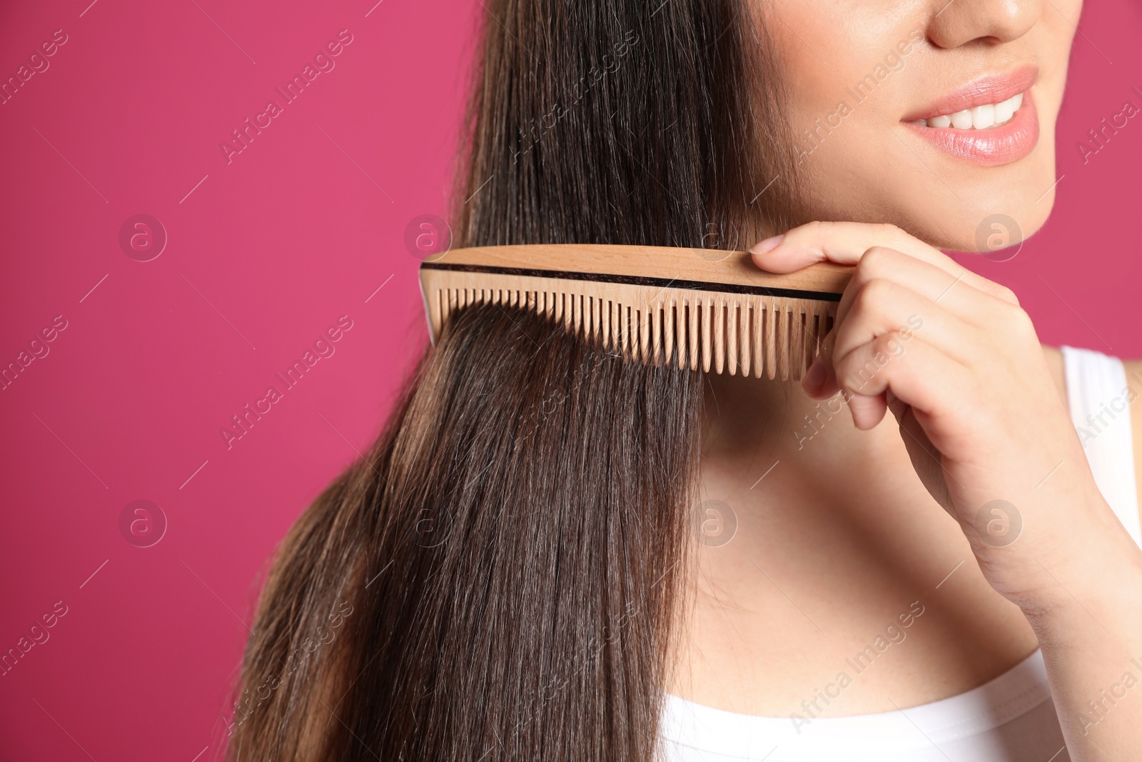 Photo of Young woman with wooden hair comb on color background, closeup. Space for text