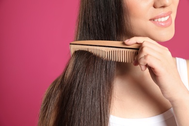 Young woman with wooden hair comb on color background, closeup. Space for text