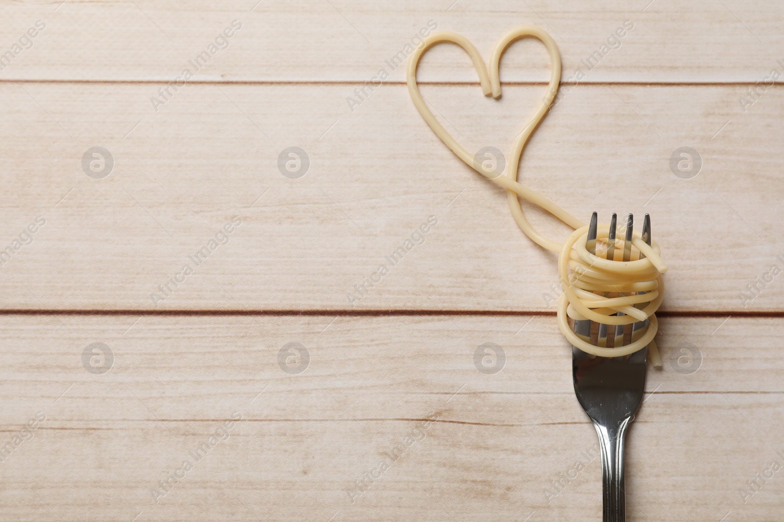 Photo of Heart made of tasty spaghetti and fork on wooden table, top view. Space for text