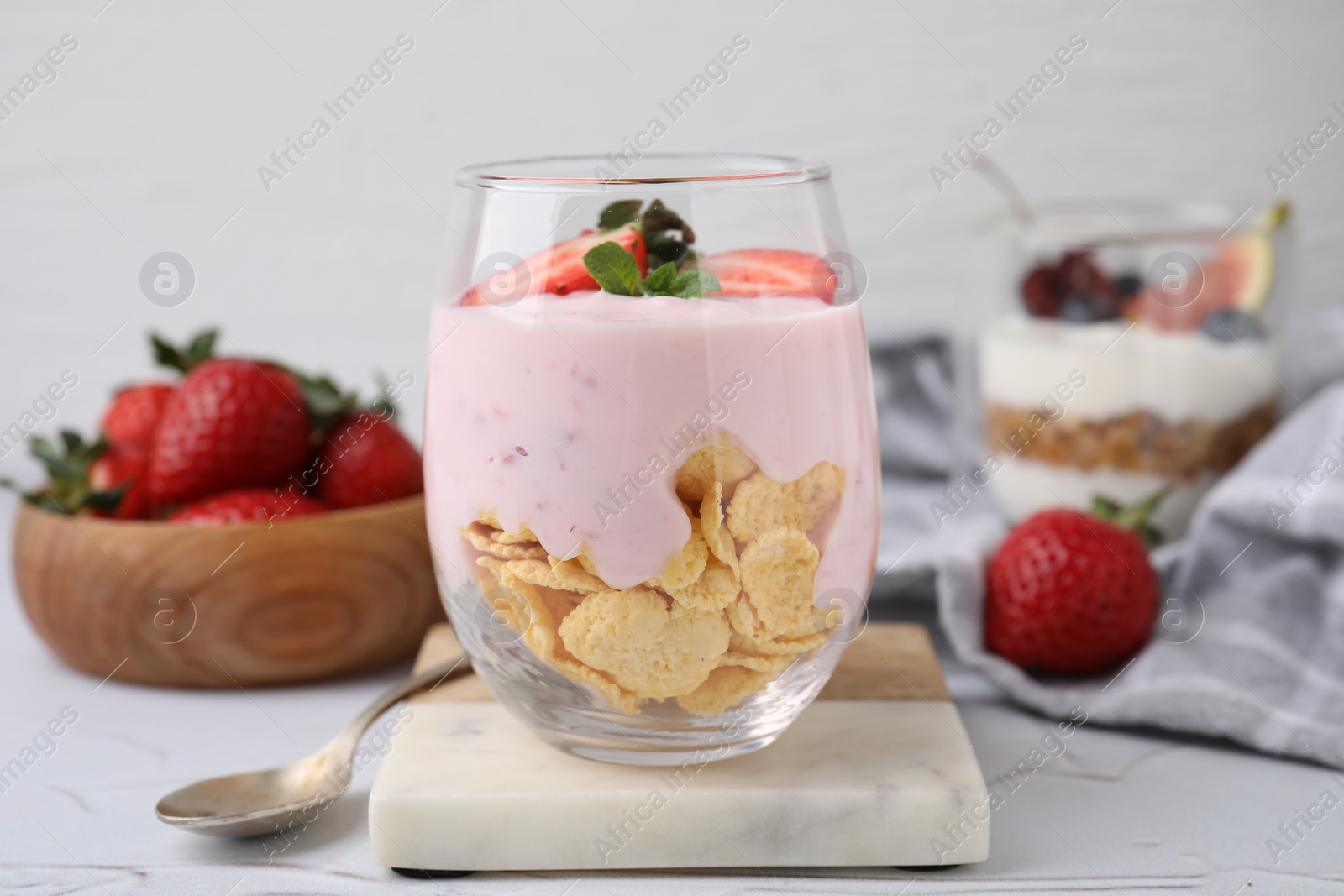 Photo of Glass with yogurt, strawberries and corn flakes on white textured table