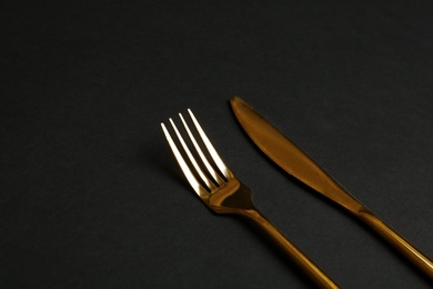 Gold fork and knife on black background. Space for text