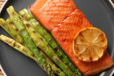 Photo of Tasty grilled salmon with asparagus and lemon on grey plate, top view