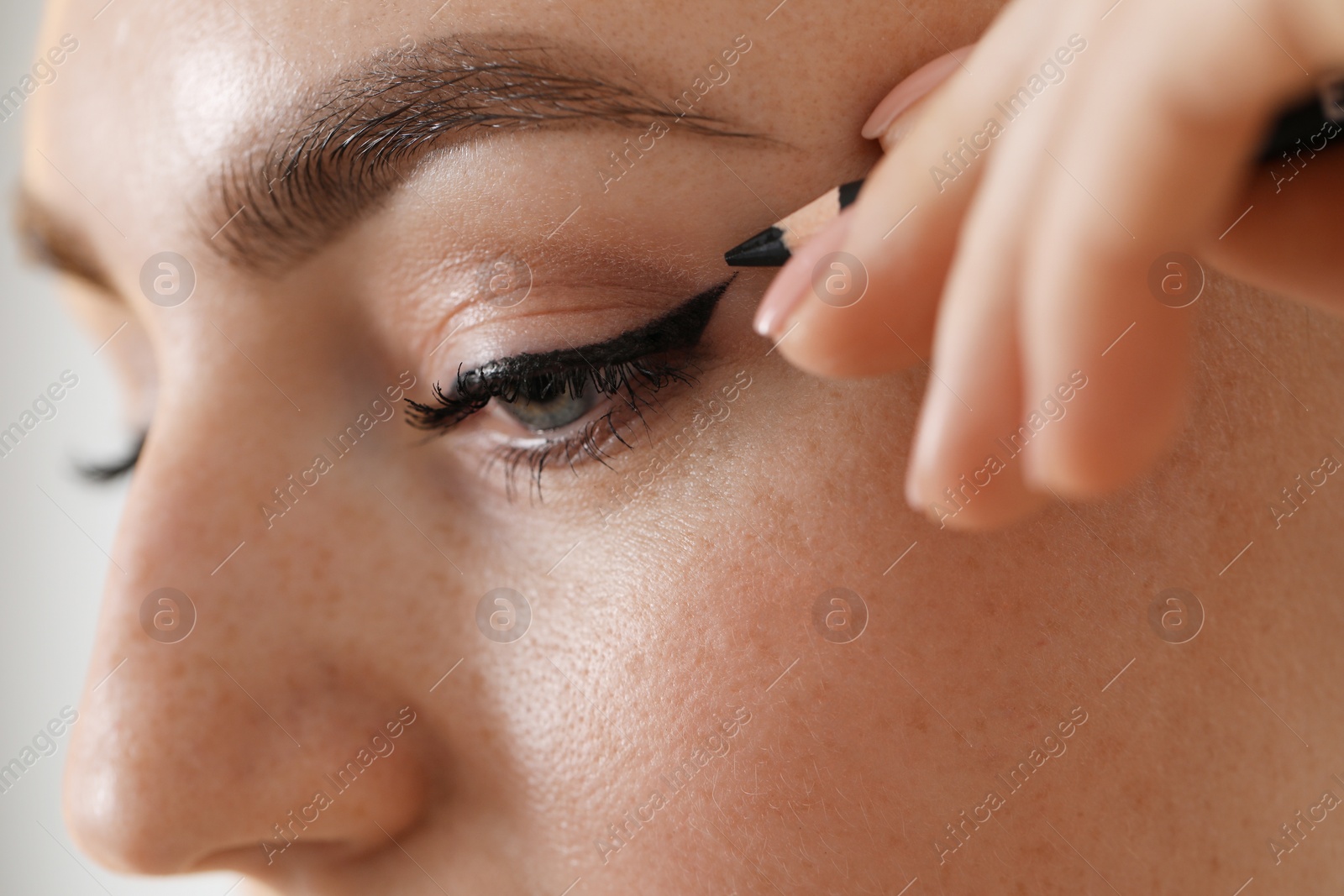 Photo of Makeup product. Woman applying black eyeliner on blurred background, closeup