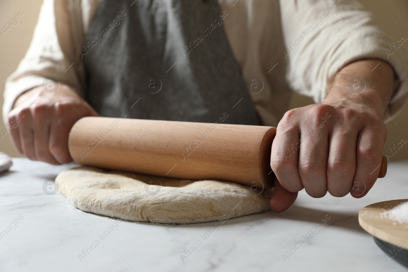 Photo of Man rolling raw dough at white table, closeup