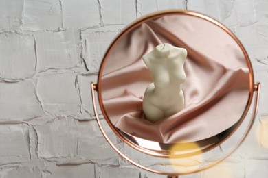 Mirror with reflection of beautiful female body shaped candle near white wall, space for text