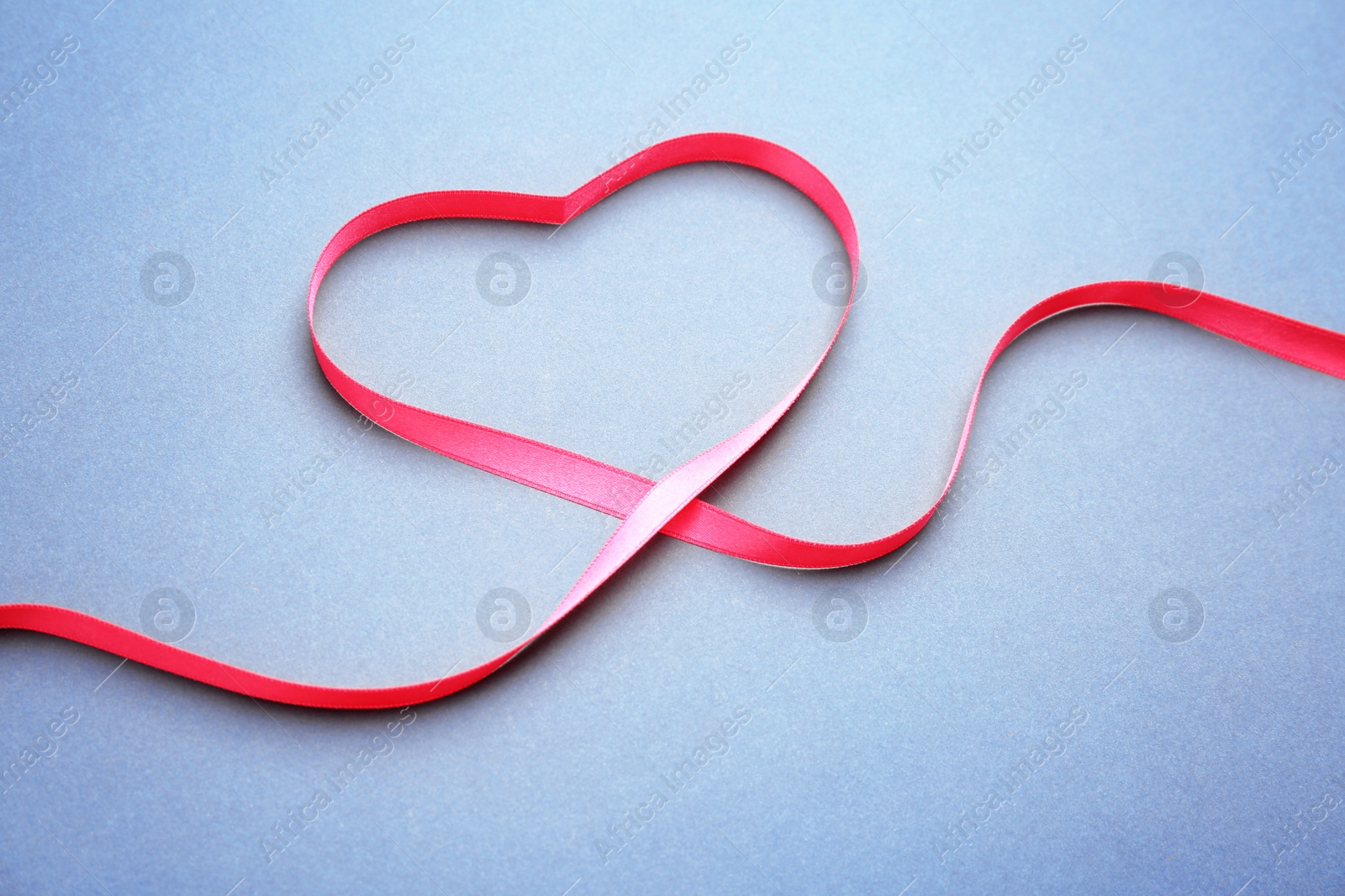 Photo of Heart made of pink ribbon on color background