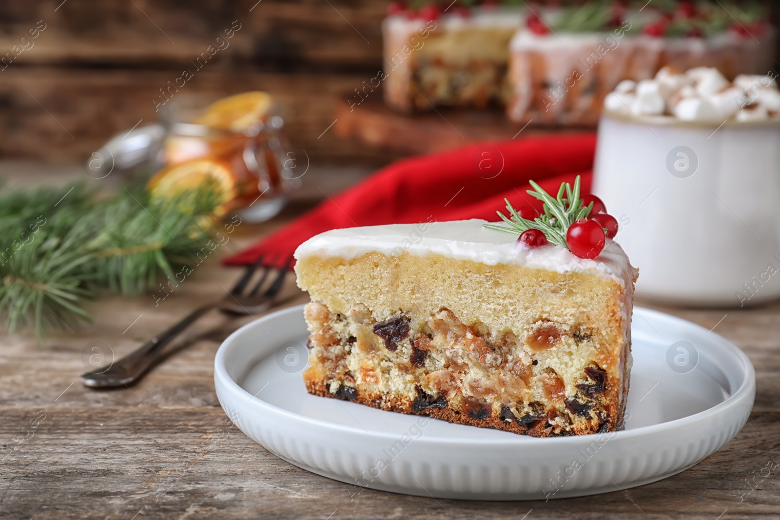 Photo of Slicetraditional Christmas cake decorated with rosemary and cranberries on wooden table