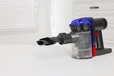 Photo of Modern vacuum cleaner on white mattress indoors. Space for text
