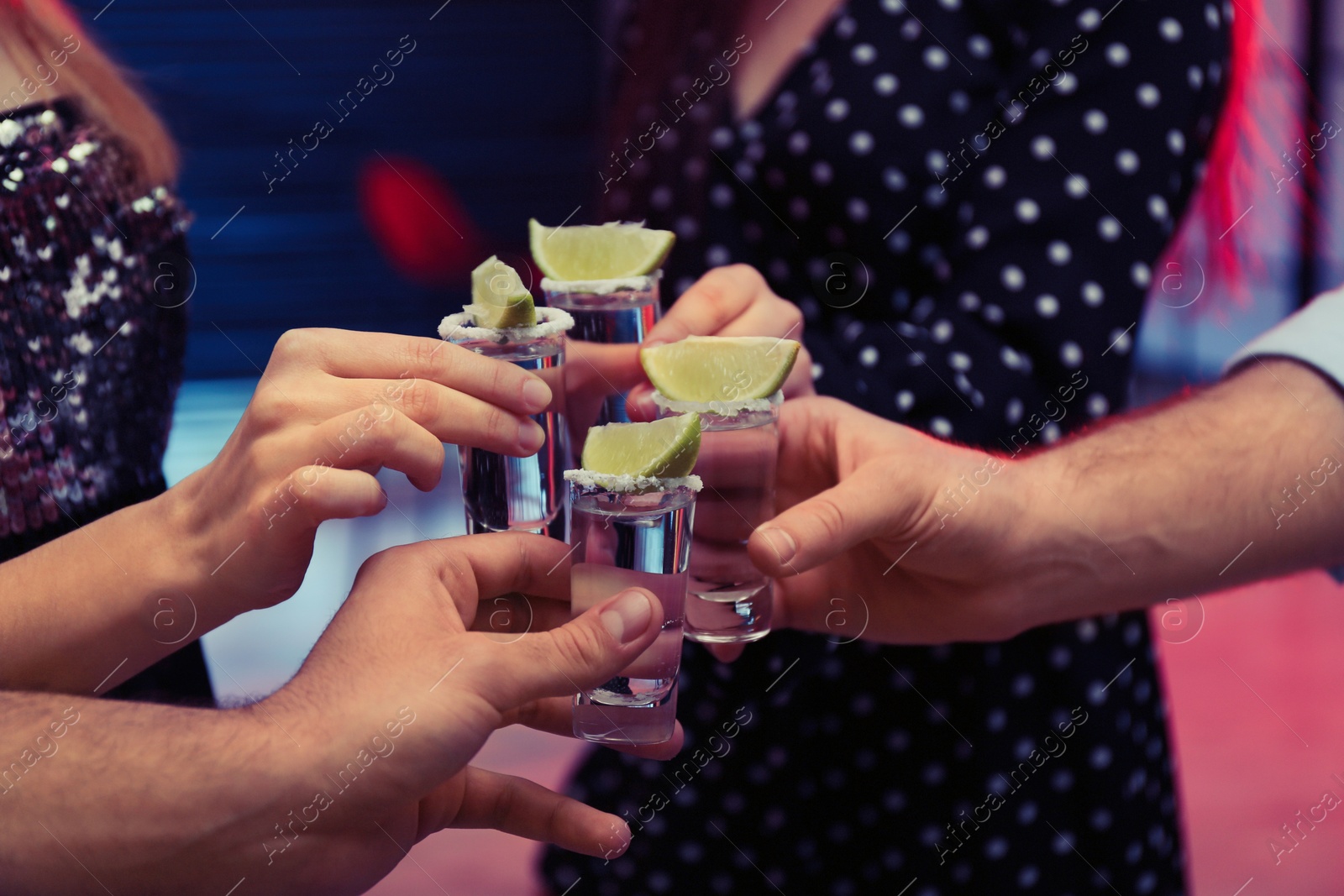 Photo of Young people toasting with Mexican Tequila shots in bar, closeup